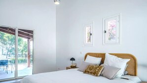 A bedroom with a large bed, a nightstand, a lamp, and a view of an outdoor patio.