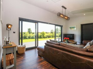 Uma sala de estar moderna com um sofá de couro, uma televisão de tela plana e uma grande porta de vidro deslizante que dá para um jardim.