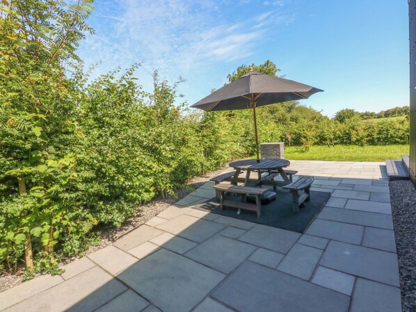 Pátio com mesa de piquenique e guarda-sol, cercado por vegetação.