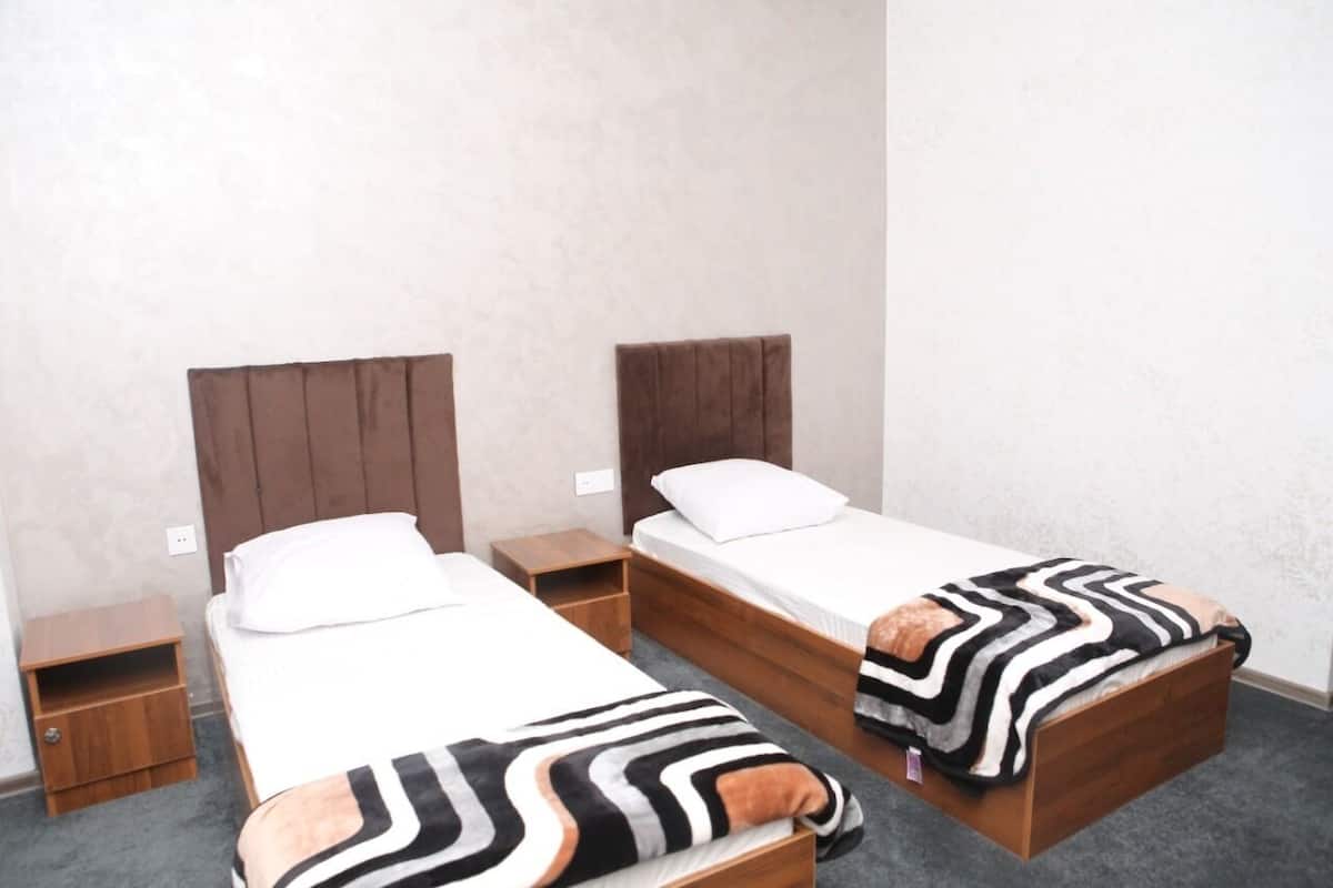 Ein Zimmer mit zwei Einzelbetten, jedes mit einem hölzernen Kopfteil und einem Nachttisch.