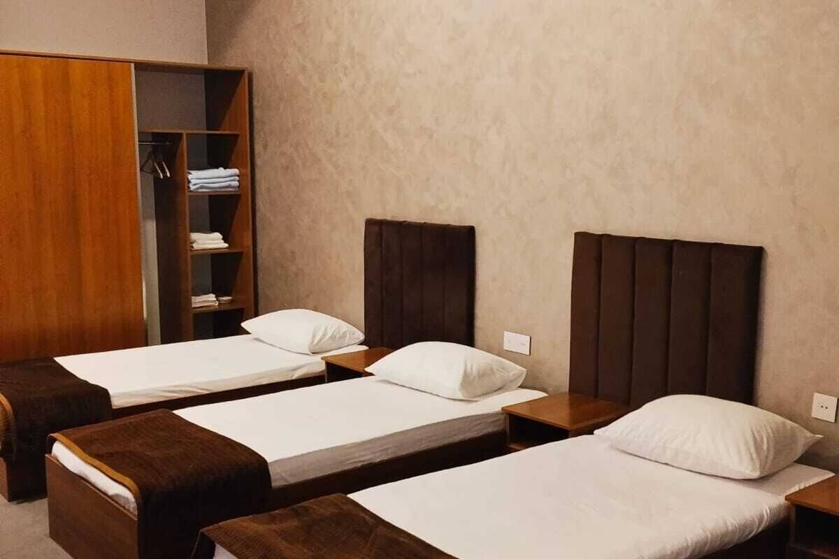 Ein Hotelzimmer mit drei Einzelbetten, einem Holzschrank und einem Einbauschrank.