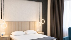 A modern hotel room with a large bed, bedside tables, a blue chair, and circular light fixtures. - Arena Hotel Tartar (Tartar)