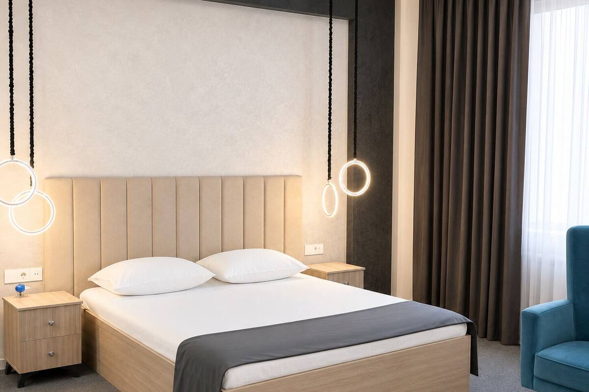 Ein modernes Hotelzimmer mit einem großen Bett, Nachttischen, einem blauen Sessel und runden Lampen.