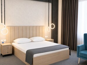 A modern hotel room with a large bed, bedside tables, a blue chair, and circular light fixtures.
