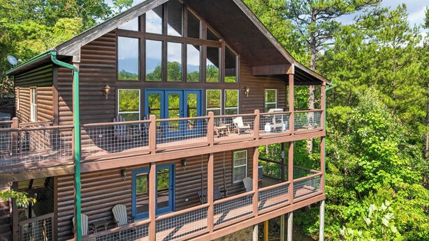 A two-story log cabin with a balcony, large windows, and a stone foundation. - 3BDR+Loft for 12 w/Hot Tub, Billiards & Mtn Views! (Sevierville)