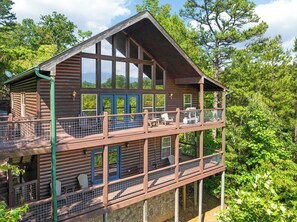 A two-story log cabin with a balcony, large windows, and a stone foundation.