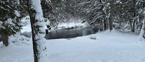 Un paysage enneigé avec une rivière, des arbres et un banc recouvert de neige.