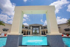 Una piscina con vista a aguas cristalinas, rodeada por un deck de azulejos y una gran estructura en arco.