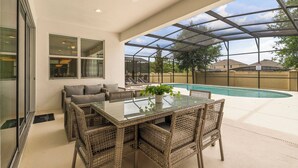 A covered patio with a glass table and wicker chairs, overlooking a swimming pool.