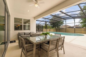 Eine überdachte Terrasse mit einem Glastisch und Korbstühlen, mit Blick auf einen Swimmingpool.