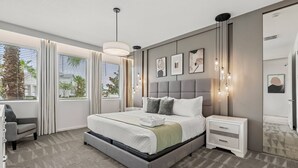 A modern bedroom with a large bed, bedside tables, a chair, and a view of the outdoors through large windows.