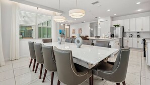 A modern kitchen with white cabinets, a stainless steel refrigerator, and a dining area with a white table and grey chairs.