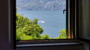 Une vue à travers une fenêtre sur un lac où se trouve un bateau, le tout entouré d’une végétation luxuriante et de bâtiments situés sur une colline.