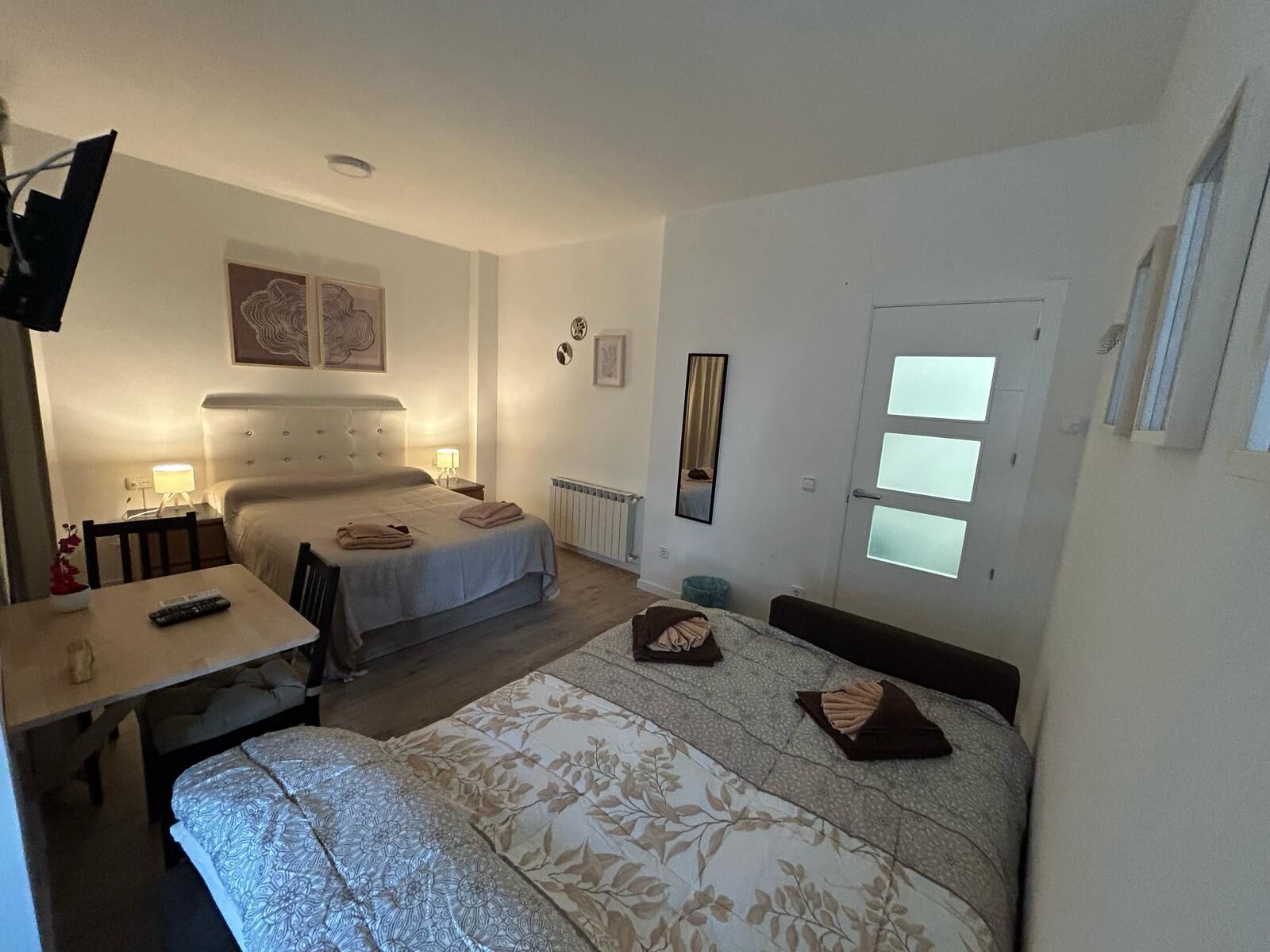 Habitación de hotel con dos camas, una mesa de comedor, una silla, un espejo y una ventana con persianas.
