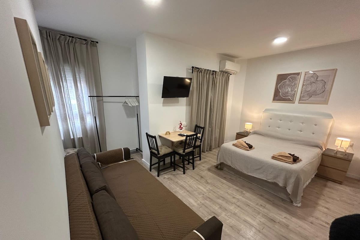 Een hotelkamer met een bed, een bank, een bureau met stoelen, een televisie en kunst aan de muur.
