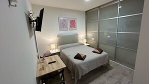 A small, modern bedroom with a bed, bedside tables, a desk, and a large window. - Habitaciones en Embajadores (Madrid)
