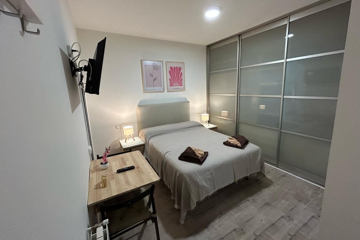 Een slaapkamer, klein en modern, met een bed, nachtkastjes, een bureau en een groot raam.