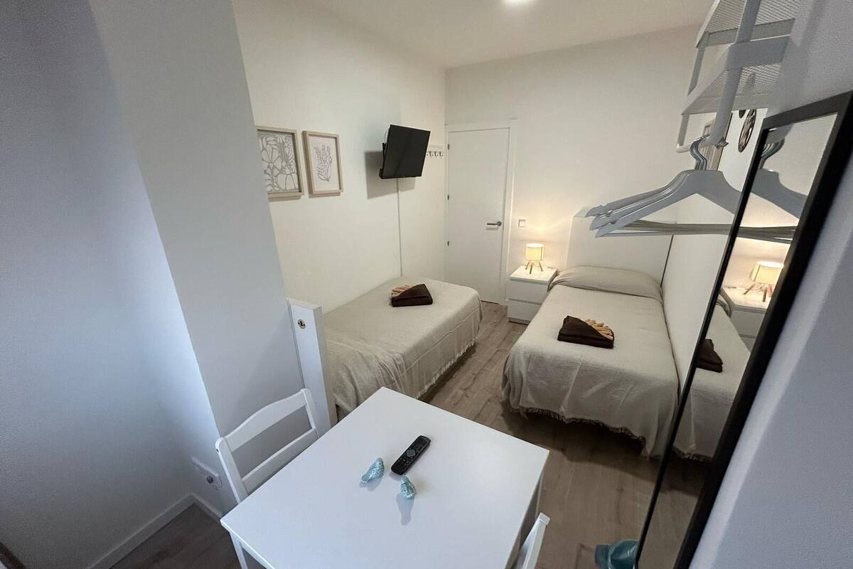 Een kleine, schone kamer met twee eenpersoonsbedden, een tafel met een afstandsbediening en een aan de muur bevestigde televisie.