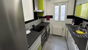 A compact kitchen with a refrigerator, stove, sink, and a window with frosted glass. - Habitaciones en Embajadores (Madrid)