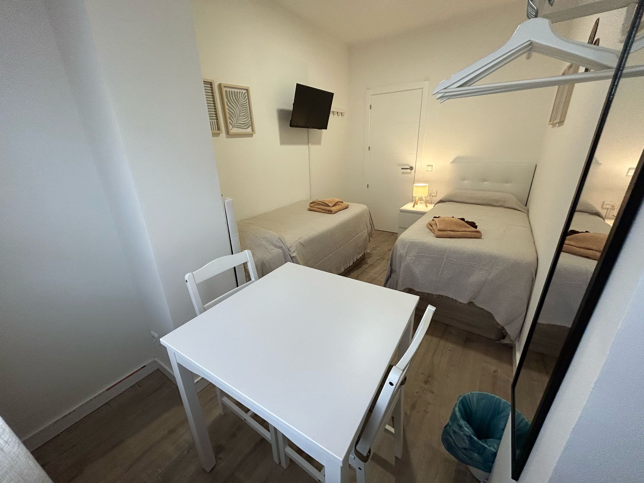 A small, clean room with a white table, two beds, a TV, and a clothes drying rack.