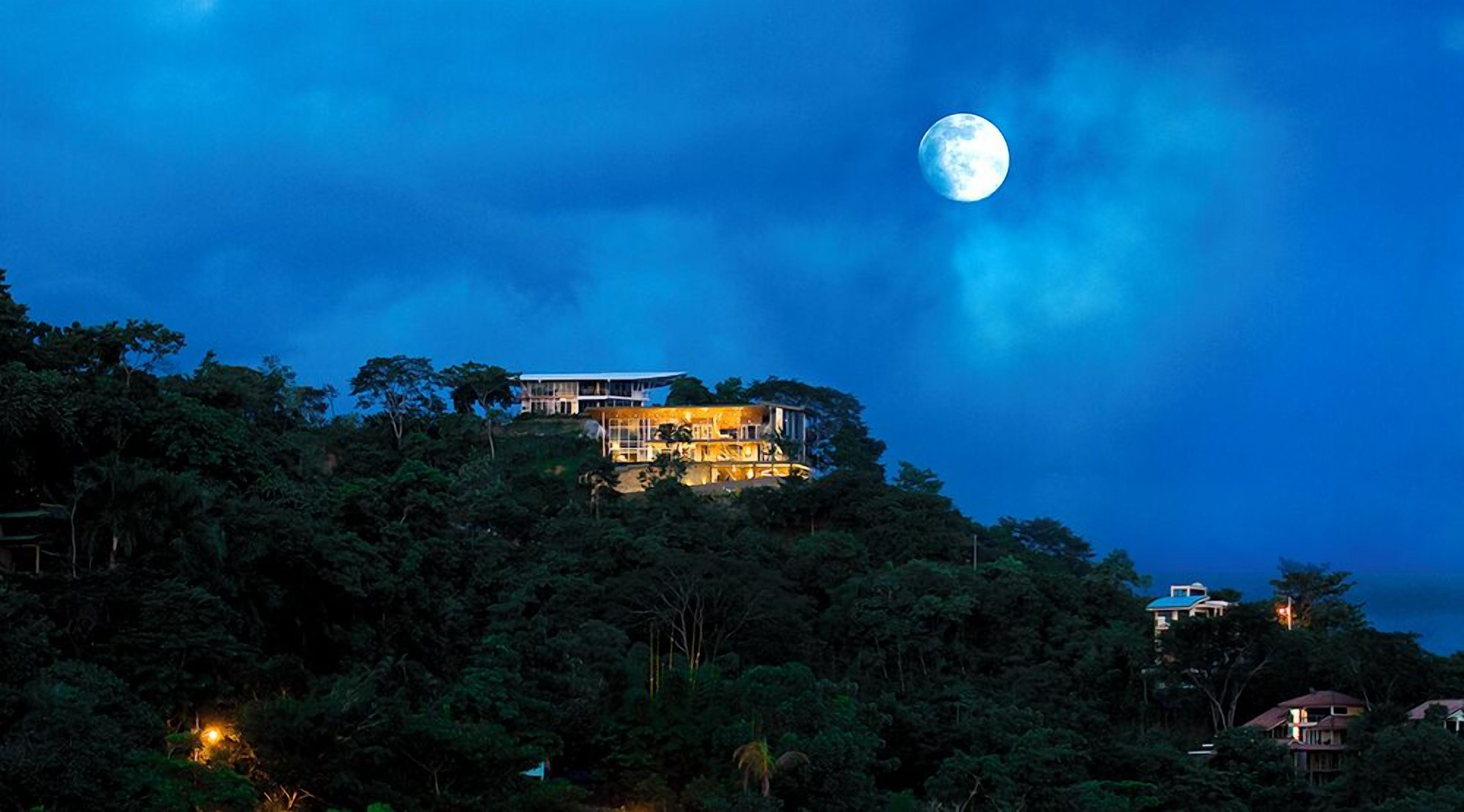 A house on a hill with a large moon in the sky.