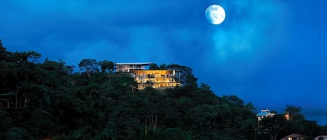 A house on a hill with a large moon in the sky.