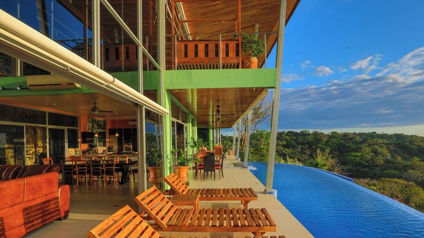 A modern hotel with a large outdoor pool, wooden lounge chairs, and a dining area with a view of the surrounding landscape. - Casa Pura Vista - Best View Home in Manuel Antonio (Manuel Antonio)