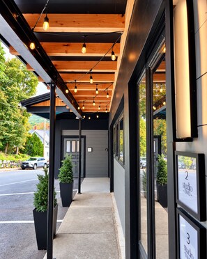 A modern building entrance with a covered walkway, potted plants, and numbered studio signs.