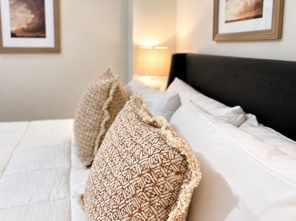Una cama bien hecha con almohadones estampados y una colcha blanca.