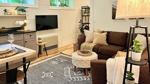 A modern living room with a flat-screen TV, a sofa, a coffee table, and a dining area with a table and chairs.