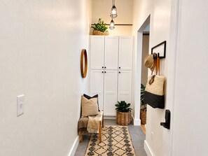 Un pasillo con un banco, un tapete estampado, una planta colgante y una cesta en la pared.