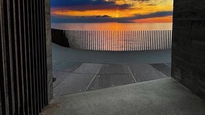 A modern architectural space with a view of a sunset over water, featuring a concrete floor and a metal fence.