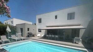 A modern pool area with a clear blue pool, lounge chairs, and a barbecue setup. - Beautiful contemporary house for 8 people (Lattes)