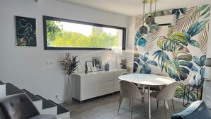 A modern kitchen with a dining area, featuring a large window, white cabinetry, and a tropical leaf mural. - Beautiful contemporary house for 8 people (Lattes)