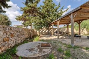 Un mur de pierre, un espace extérieur abrité avec des tables et des chaises, et un grand arbre.