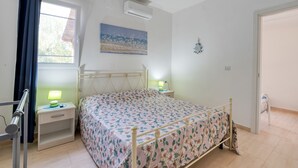 Un dormitorio con cama, mesitas de noche, una ventana con cortinas, aire acondicionado y un cuadro en la pared.