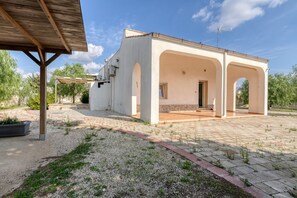 Un bâtiment blanc doté d’un patio couvert, d’un chemin de gravier et d’une pergola en bois.