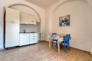 A compact kitchen with white cabinets, a dining table with blue chairs, and a painting on the wall.