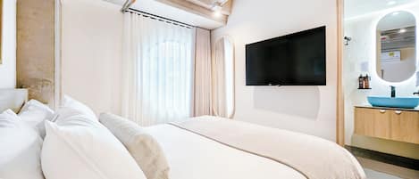 Una habitación de hotel moderna con una cama grande, un televisor de pantalla plana en la pared, un baño con un lavamanos azul y un espejo amplio.