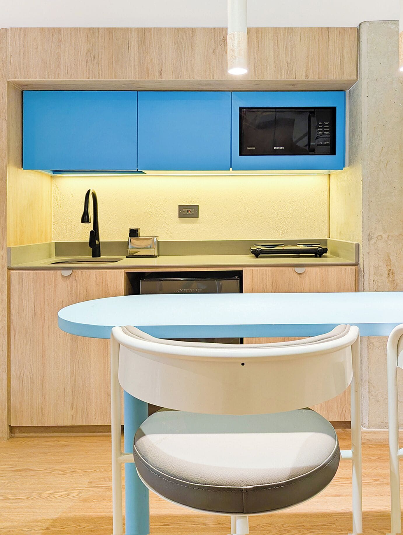 A compact kitchen with blue cabinets, a microwave, a sink, and a small dining table with chairs.
