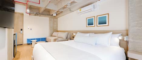 A modern hotel room with a large bed, a flat-screen TV, a small table, and a blue bench.