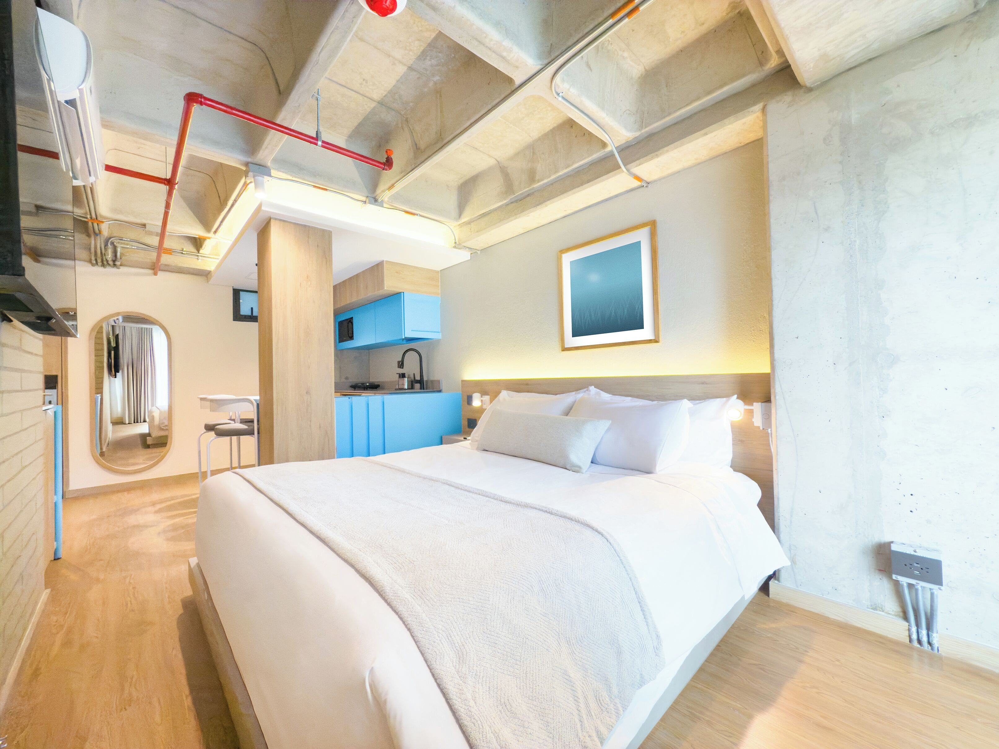 A modern hotel room with a large bed, a built-in kitchen, and a bathroom.