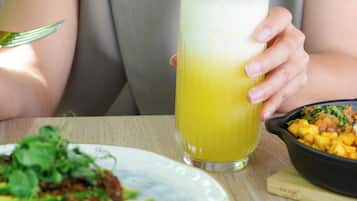 Una persona sosteniendo un vaso alto de una bebida amarilla, un plato con ensalada y un tazón de fruta.