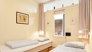 A bedroom with two single beds, a window with a view of a brick building, and a framed picture on the wall.