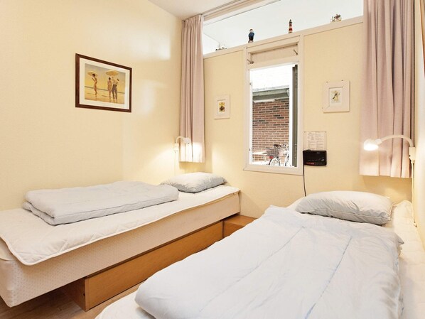 Un dormitorio con dos camas individuales, una ventana con vista a un edificio de ladrillo y un cuadro en la pared.