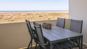 A balcony with a table and chairs overlooking a beach.