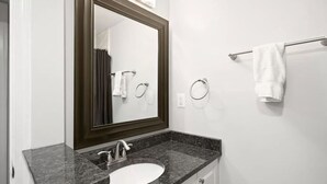 Un baño con un espejo de marco oscuro, un lavabo blanco y un perchero para toallas.