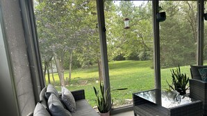 Eine überdachte Terrasse mit einer Couch, Kissen und Topfpflanzen.