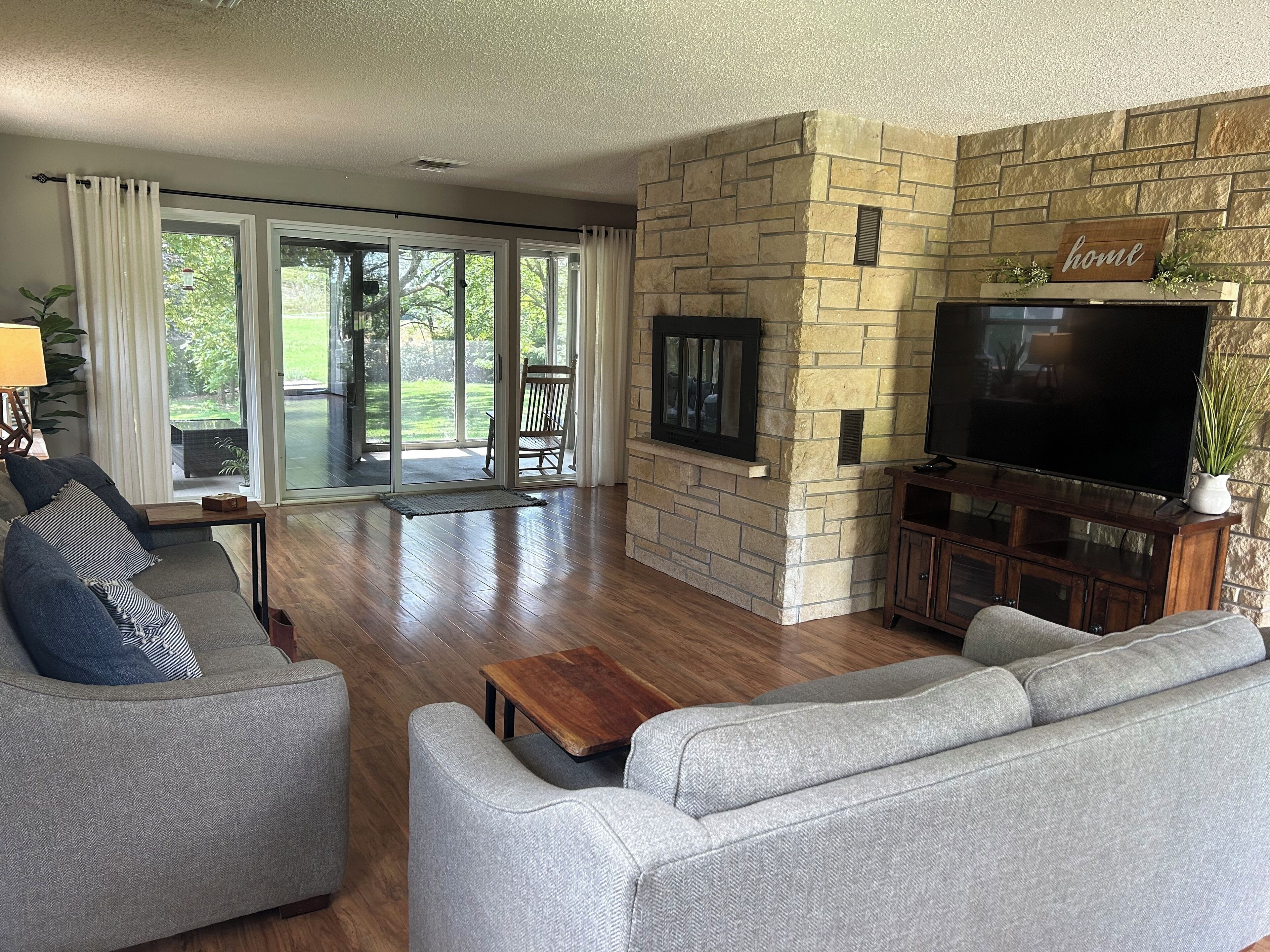 A living room with a stone fireplace, a flat-screen TV, a sofa, and a sliding glass door leading to a patio.