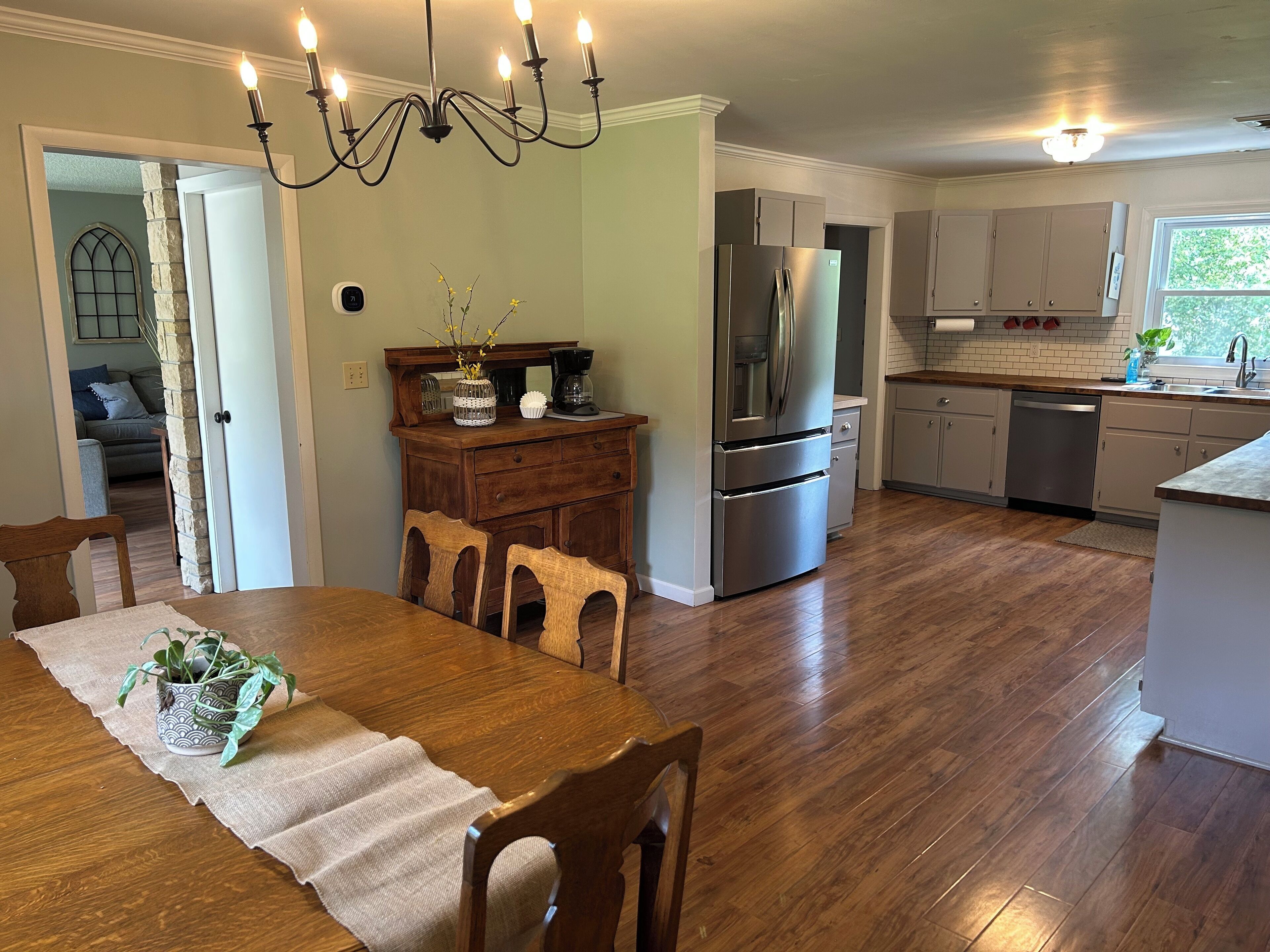 A modern kitchen with a dining area, wooden flooring, and a chandelier.